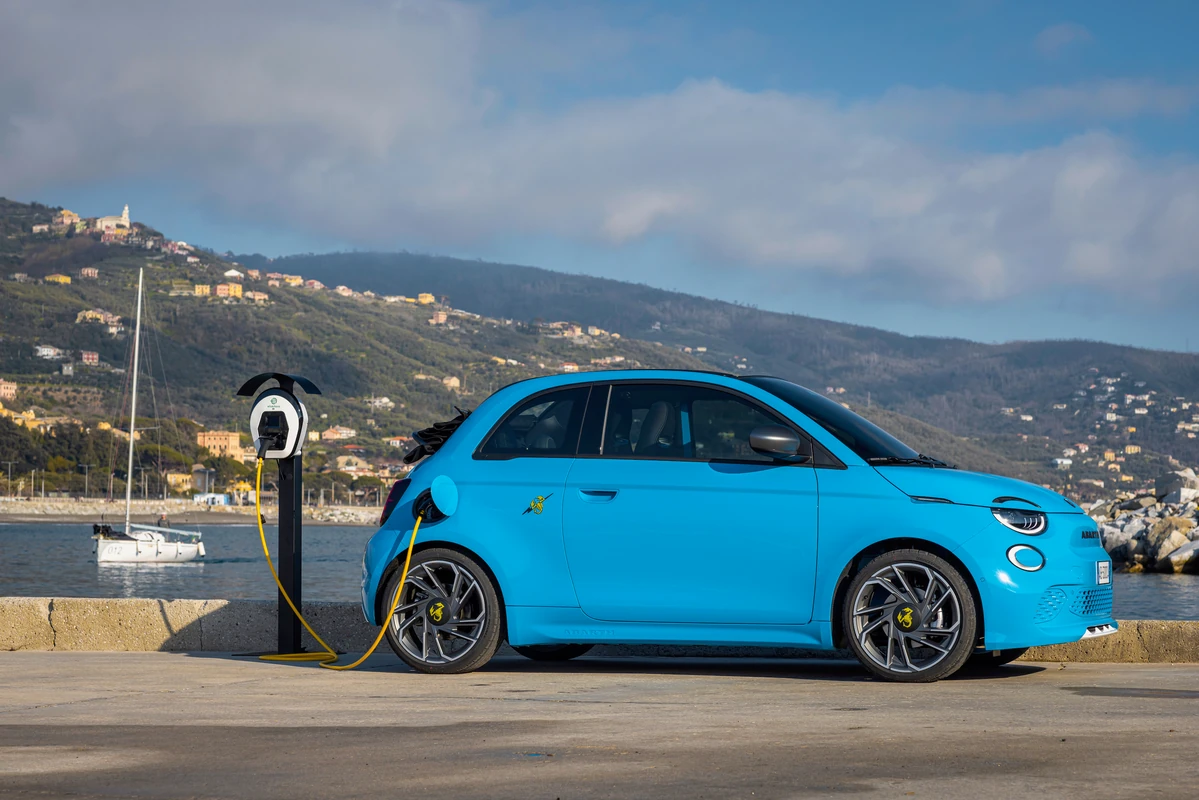 Abarth 500e cargando en punto de recarga público con vistas al mar, ejemplo de movilidad eléctrica integrada en el estilo de vida
